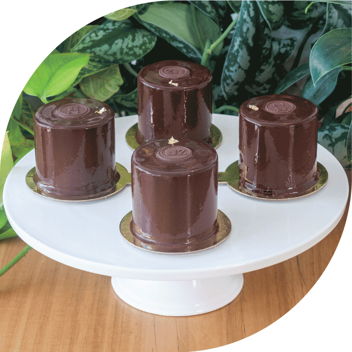 four sachertorte petits gateaux on a white cake stand in front of greenery