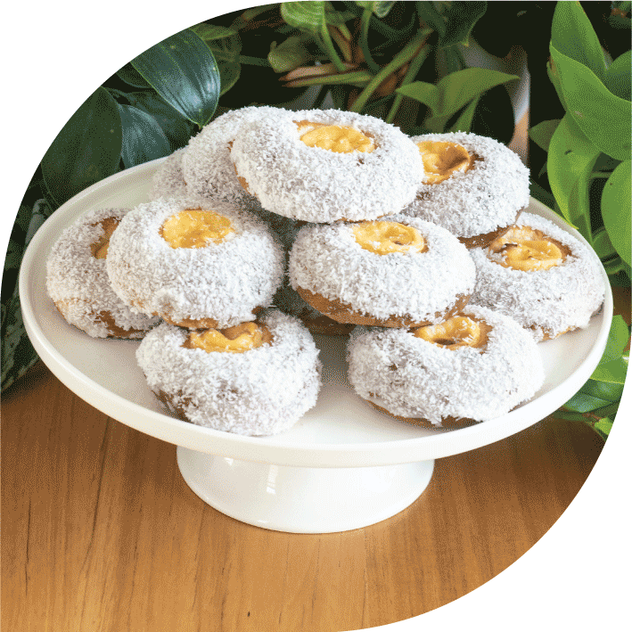 a pile of norwegian cardamom, custard and coconut buns on a white cake stand in front of plants