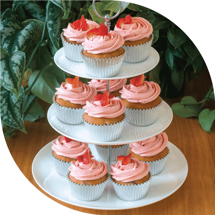 a white three tiered high tea stand with 12 pink strawberry cupcakes decorated with fresh strawberries on top of pink buttercream